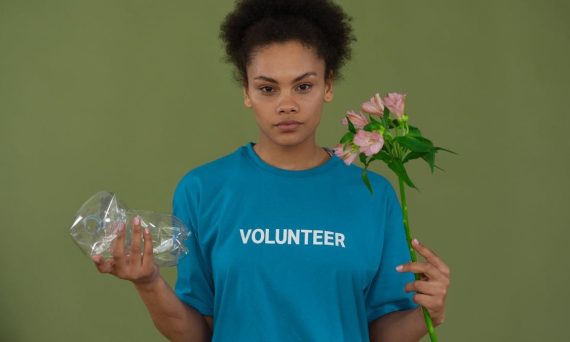Portrait of a volunteer promoting environmental conservation, holding recycled plastic and flowers.