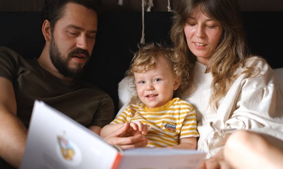 A happy family reading together, featuring parents and their smiling child enjoying a book indoors.