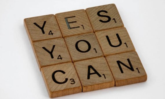 Wooden Scrabble tiles on white surface spelling 'Yes You Can,' promoting positivity and motivation.